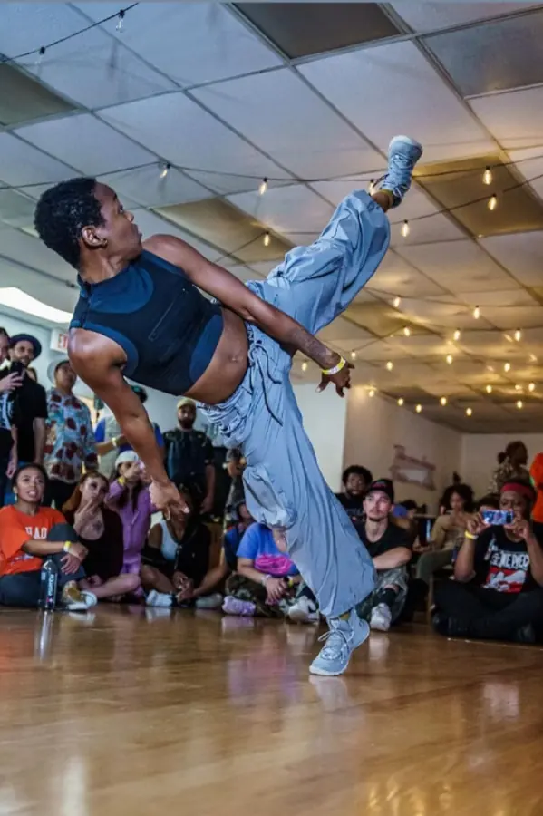 JustBee mid-kick in a dance battle circle, crowd watching