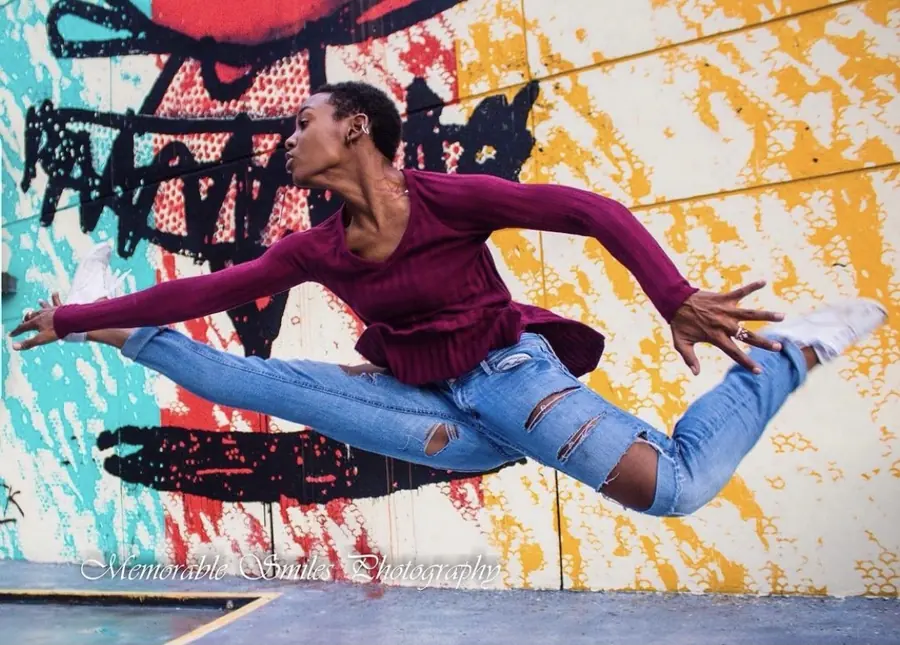 JustBee in a split leap in front of a painted mural