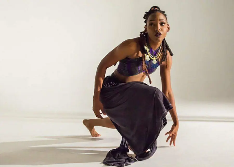 JustBee crouched low in a dance pose under studio light