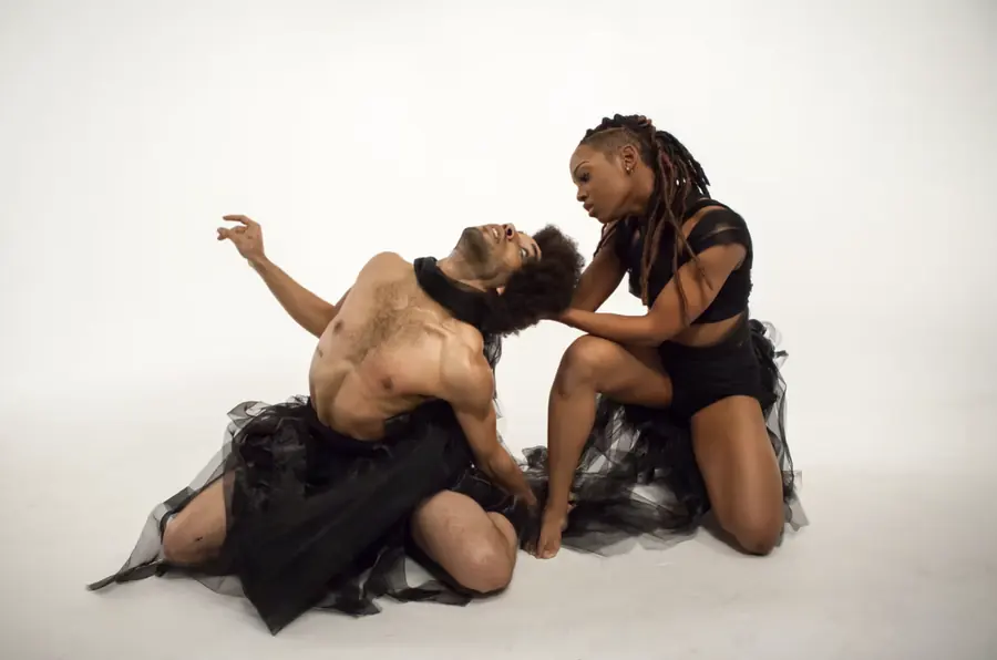 JustBee kneeling and cradling her partner's head as he arches back