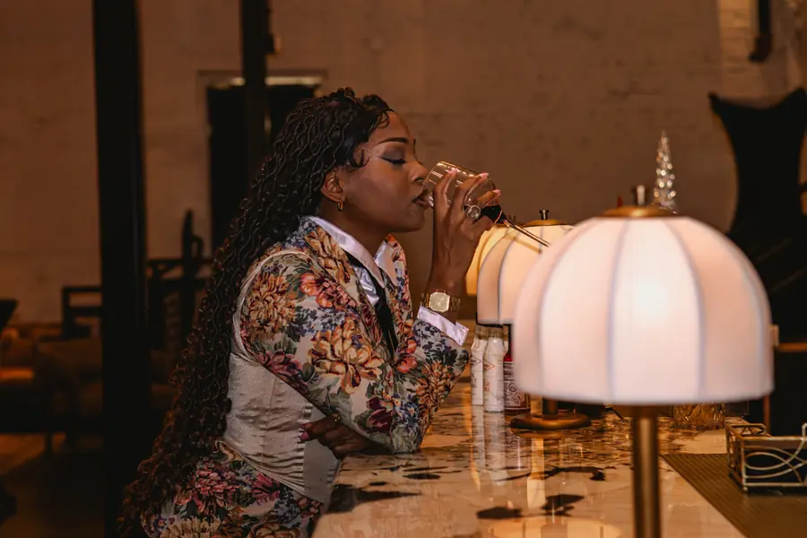 JustBee sipping wine at a marble bar in a floral suit