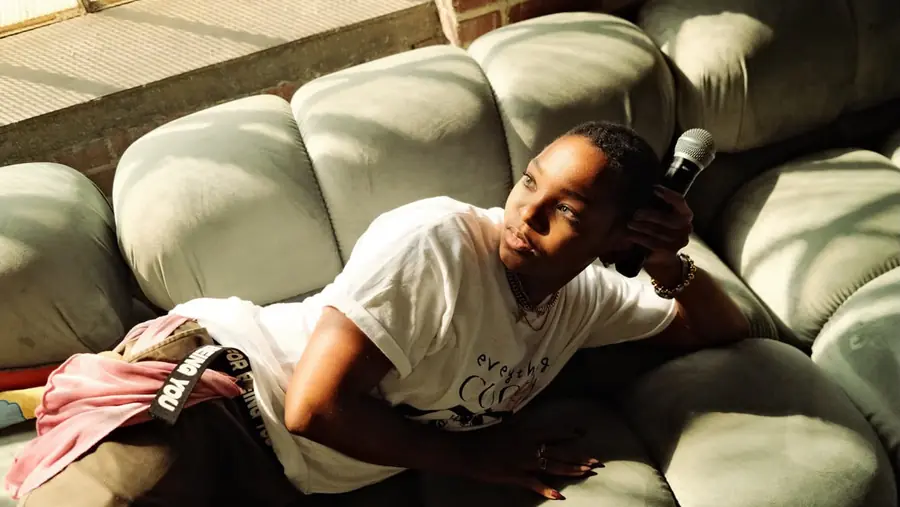 JustBee resting on a sofa, microphone in hand