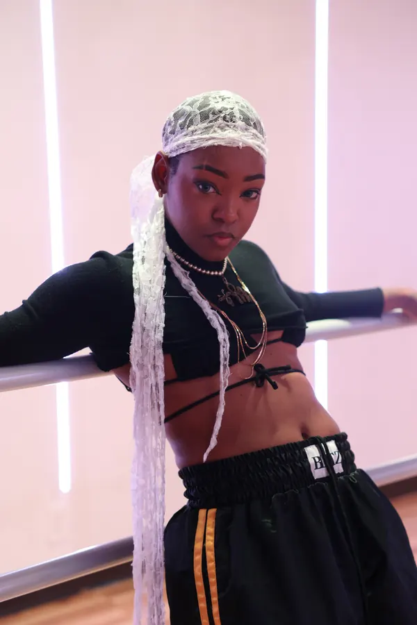 JustBee in a lace durag leaning on a dance barre