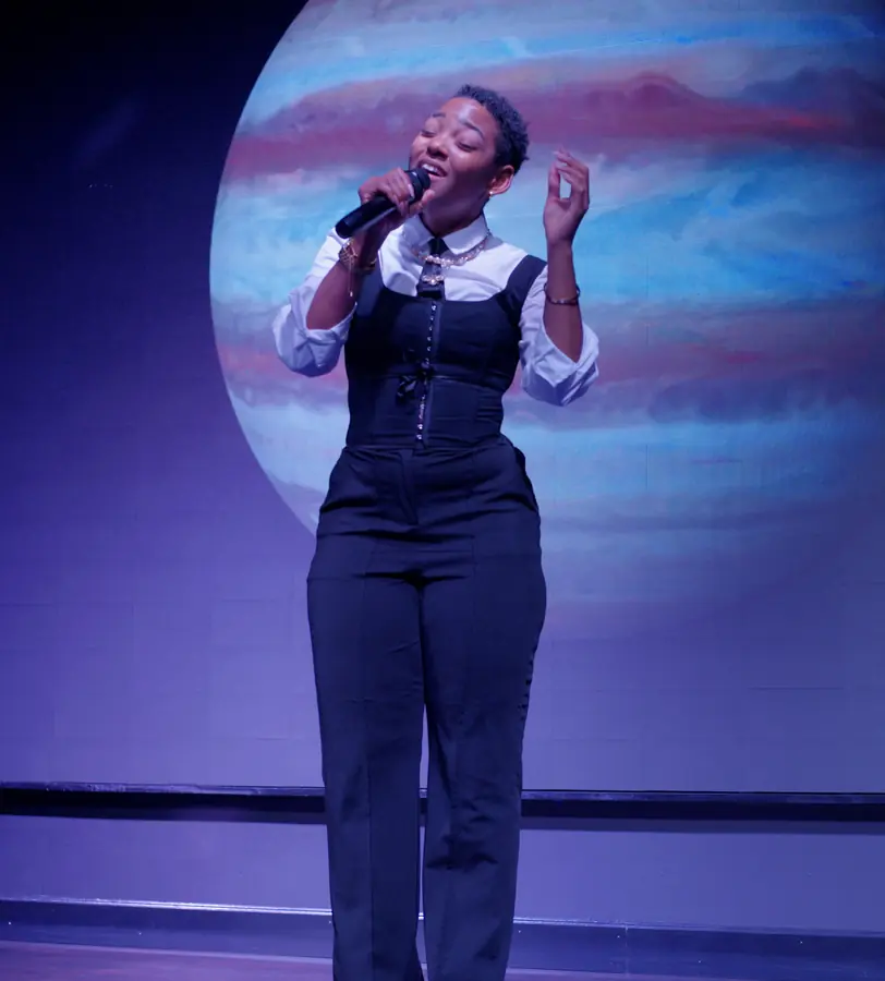 JustBee singing in front of a giant planet backdrop at Sweet Serenade