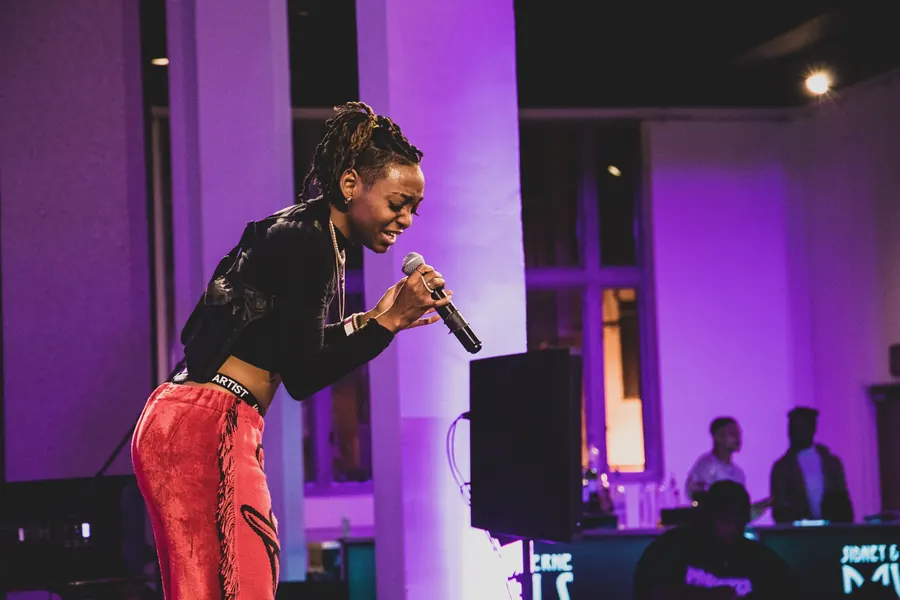 JustBee belting into a microphone on a purple-lit stage