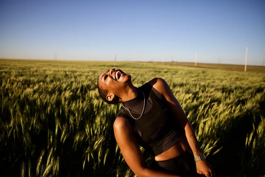 JustBee laughing with her head thrown back in a wheat field