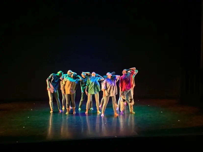 Young dancers in a colorful group pose on stage at a summer arts camp production